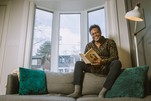 man sitting on a couch in front of a window holding a book and smiling