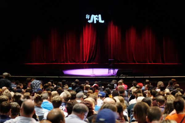 stage with the letters "JFL" appearing in front of a live audience